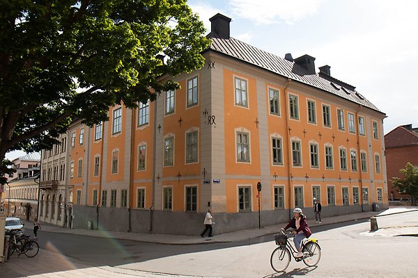 Några personer går och cyklar utanför ett trevåningshus med orange fasad