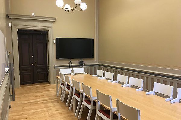 A seminar room with a table, chairs and a brown door.