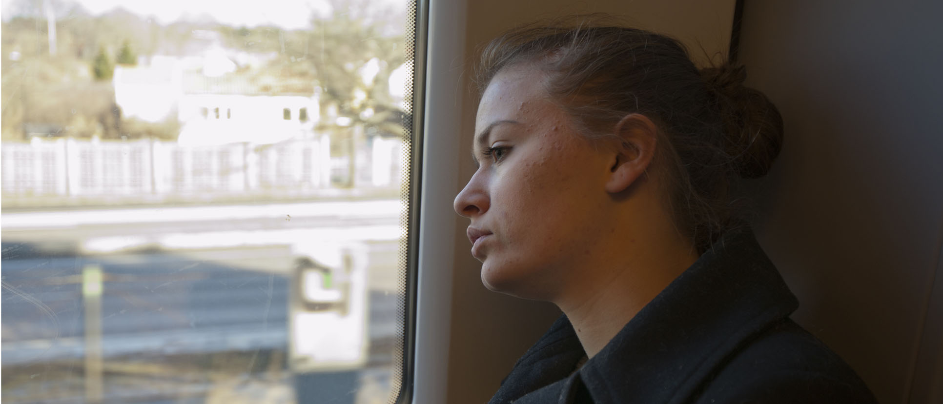 Kvinna som sitter på ett tåg och tittar ut med sorgsen blick.