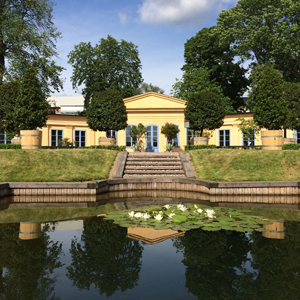 The yellow orangery in the Linnaeus Garden with a pond with water lilies in front of it.