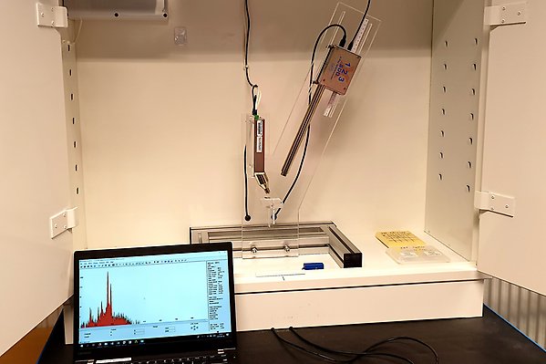 XRF set-up in a cabinet. X-ray source, detector and sample holder are mounted to a Plexiglas frame. A laptop showing a measured spectrum is standing in the front. A laptop showing a measured spectrum is standing in the front.