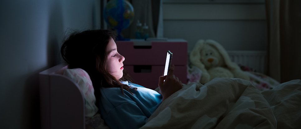 Girl lying in bed in a dark room watching her mobile phone.