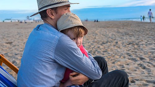 A man hugging a child on a beach.