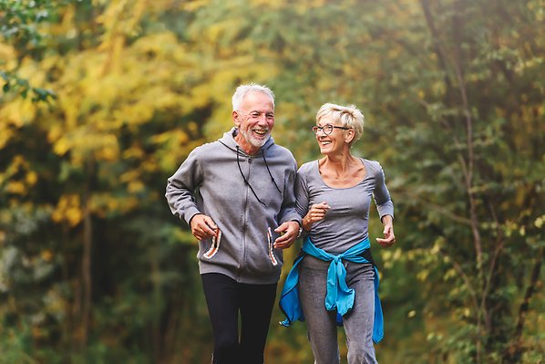 An older man and woman jogging in the forest.