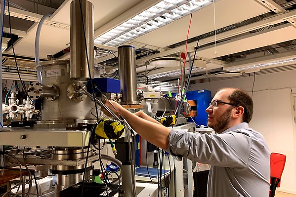 Experimental set-up in a laboratory that consists of a beamline and a vacuum chamber. A man works on the vacuum chamber.