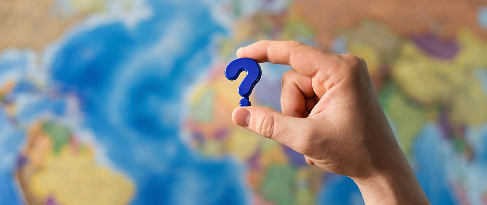 Hand holding a question mark in front of a world map