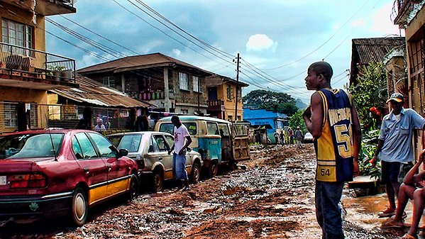 En lerig gata i Sierra Leone, med bilar parkerade längst vägen och hus i bakgrunden.