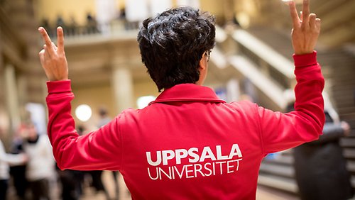 Studentambassadör gör peacetecknet med båda händerna. Hen har på sig en röd tröja med texten Uppsala universitet på.