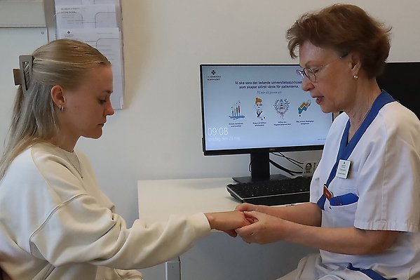 En kvinnlig läkare undersöker en ung kvinnlig patients hand.