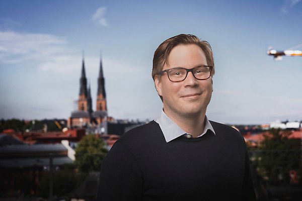 John med glasögon mot en Uppsalabakgrund med Domkyrkans torn
