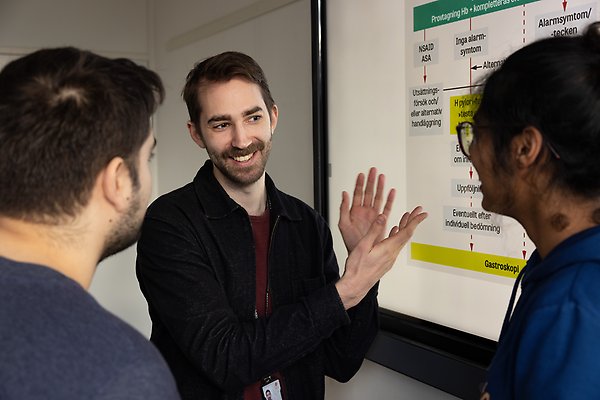 En lärare pekar på en skärm med text framför två studenter