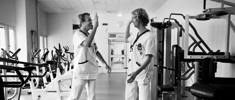 Två manliga fysioterapeuter som high fivear varandra inne på ett gym.