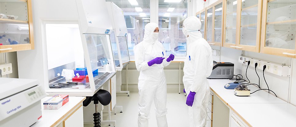 Två personer står och jobbar i ett labb med skyddskläder på