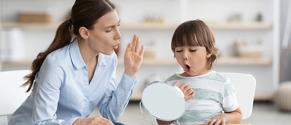 Kvinna och barn formar ljud framför liten spegel.