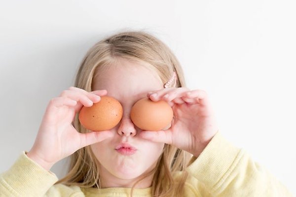A child is holding two eggs in front of their eyes