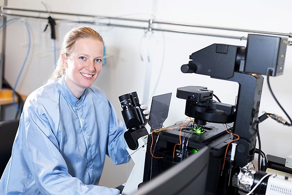 Kvinna i labbrock kollar i mikroskop