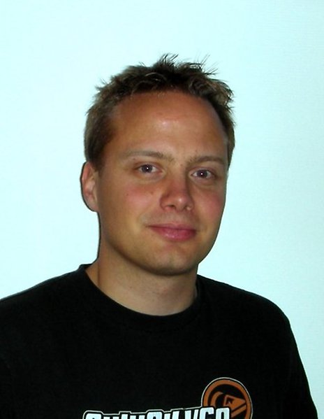 Porträttbild av Thomas i svart tröja mot enfärgad bakgrund.