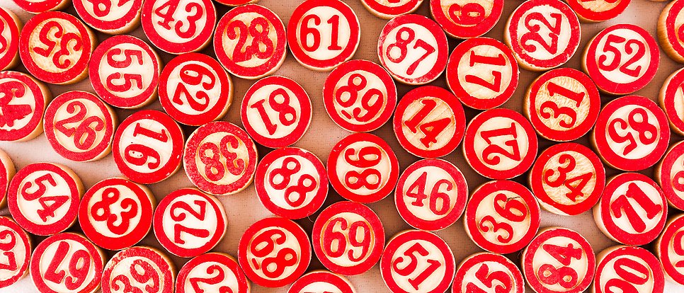 Bilden är en metafor för lotteri: Ett stort antal röda stämplar med olika nummer ligger slumpvis utlagda.