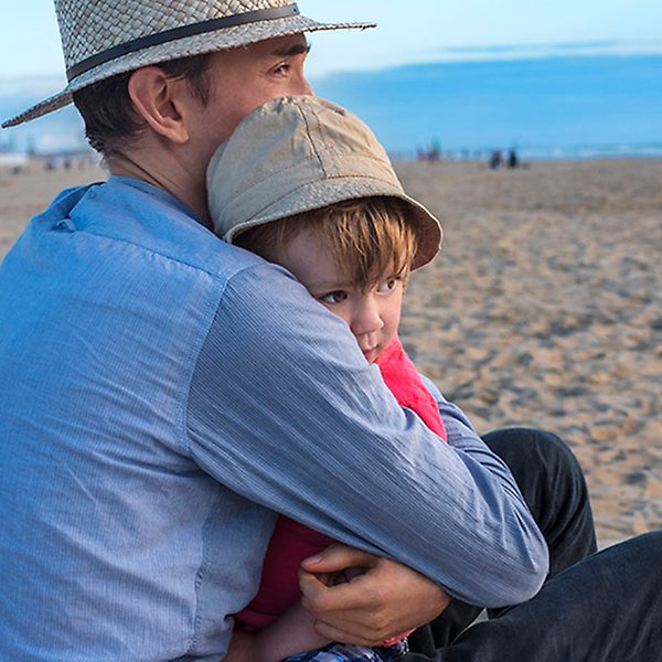 En man kramar ett barn på en sandstrand.